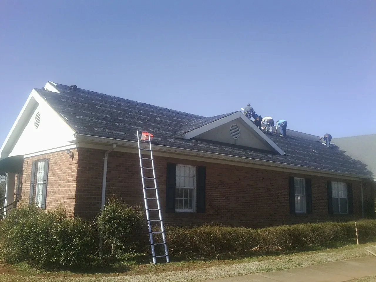 Crew tearing shingles off a brick ranch roof with a ladder set — Emergency Roof Repair work by our crew in Rochelle
