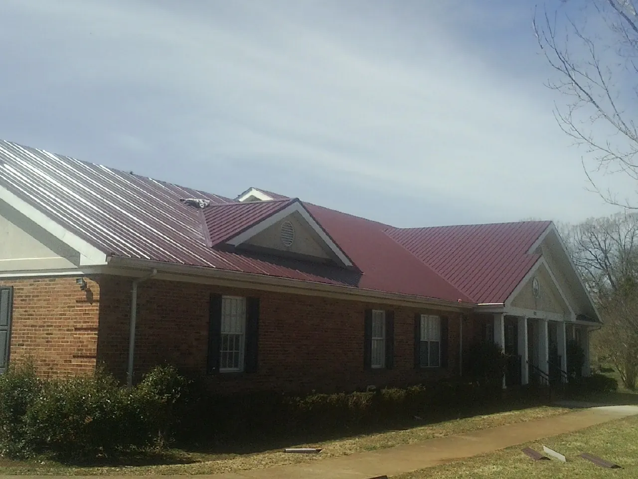 Red metal roof with gabled entries on a long brick building, from a Hail Damage Roof Repair job in Rochelle