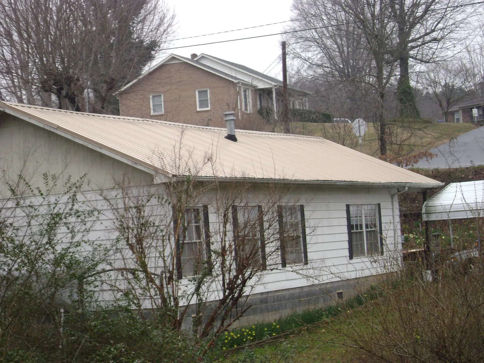 Tan metal roof on a white sided house set into a hillside — Commercial Roofing by Roofing Brothers in Rochelle