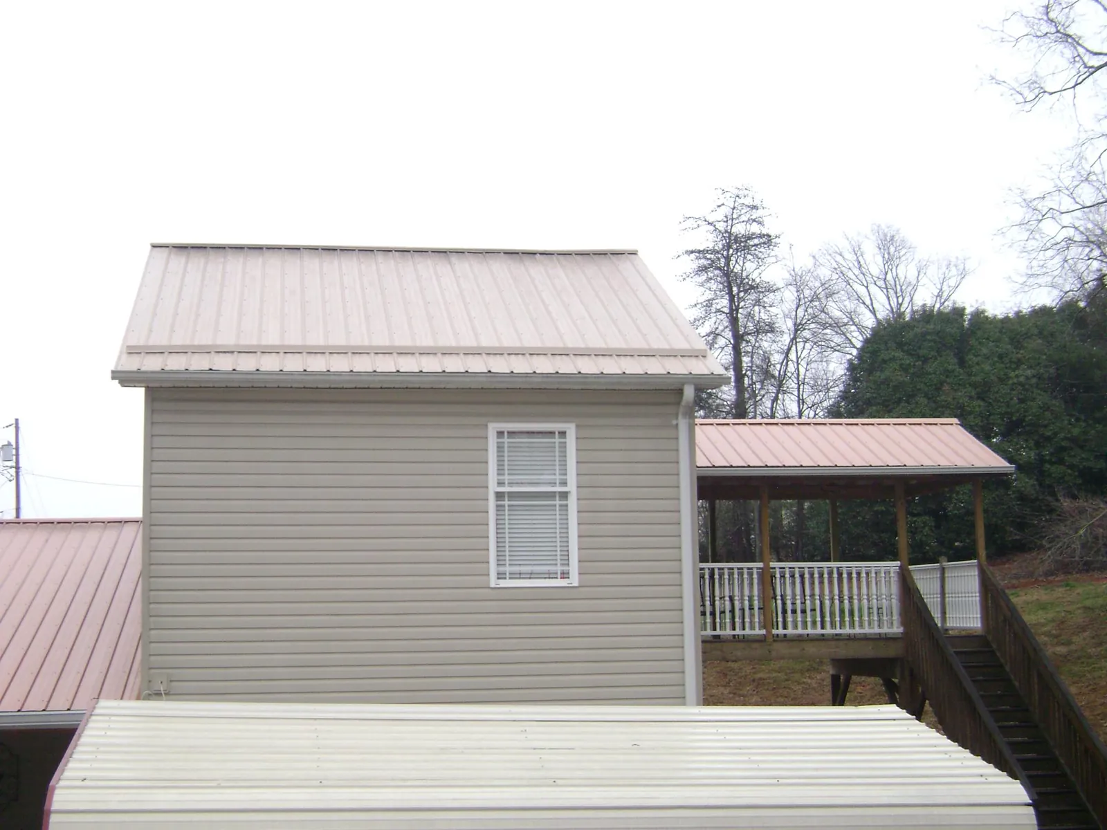 Tan metal roofs on a two story addition and attached porch, from a Roof Replacement job in Rochelle